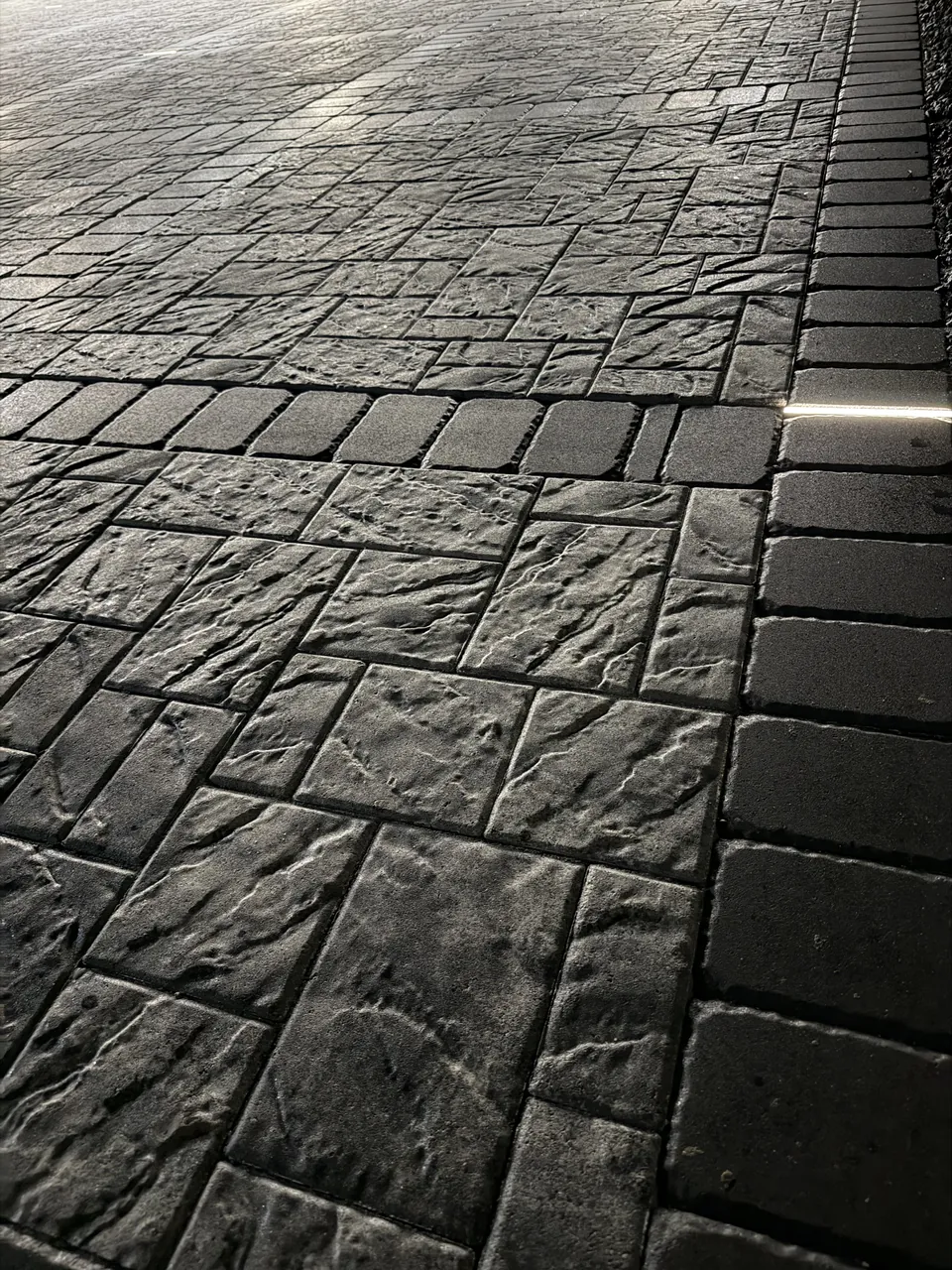 Close-up of charcoal slate-texture pavers with a soldier-course border, showing joint alignment and surface relief