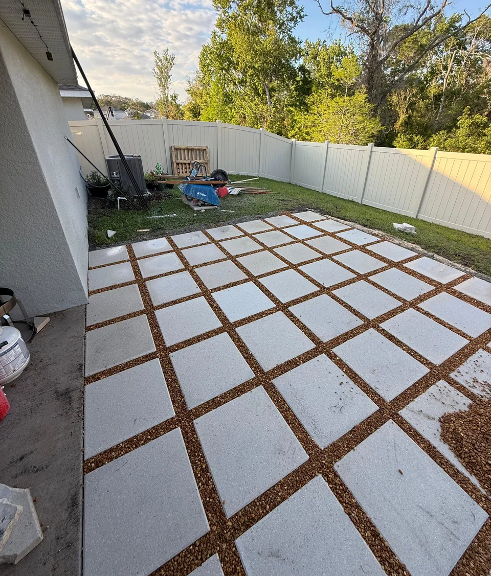 Backyard patio built from large square concrete pavers set on a compacted base with gravel-filled joints