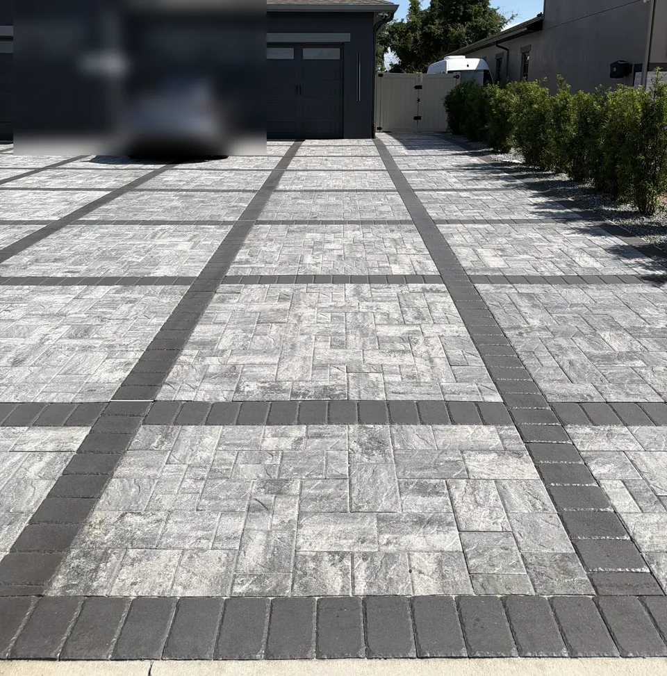 Gray paver driveway with charcoal banding leading to a dark two-car garage, with a matching paver walkway alongside