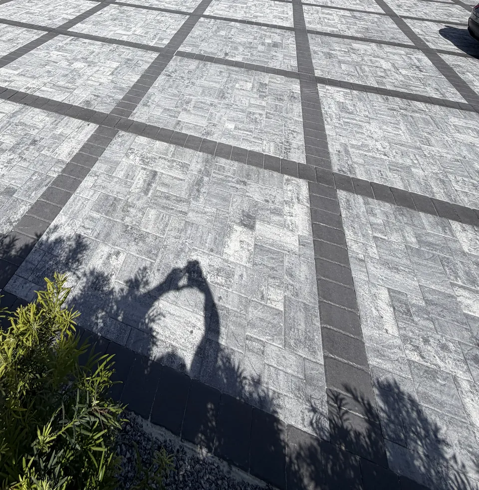 Wide gray paver driveway with a charcoal grid and border pattern running from the street to a two-car garage