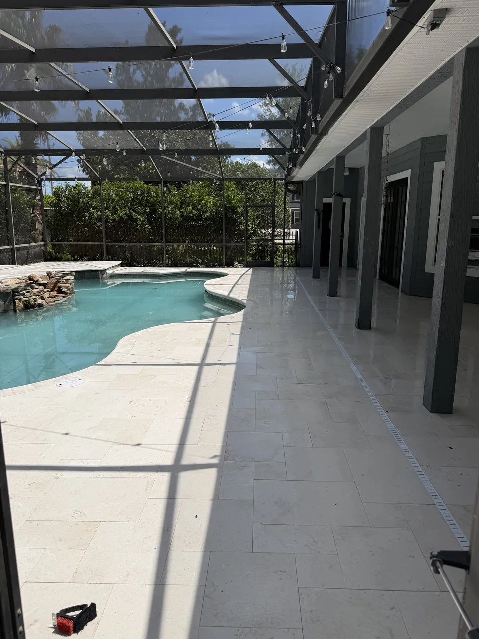 Screened lanai with a full marble paver pool deck, drainage channel, and freeform pool with rock waterfall