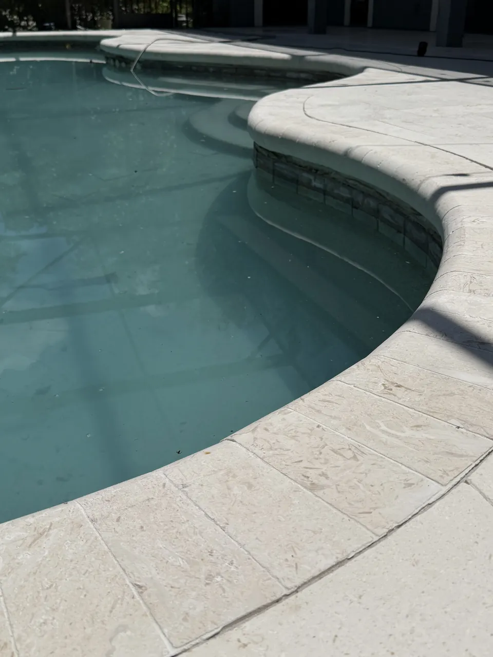 Bullnose marble pool coping and matching marble deck pavers around a curved pool edge