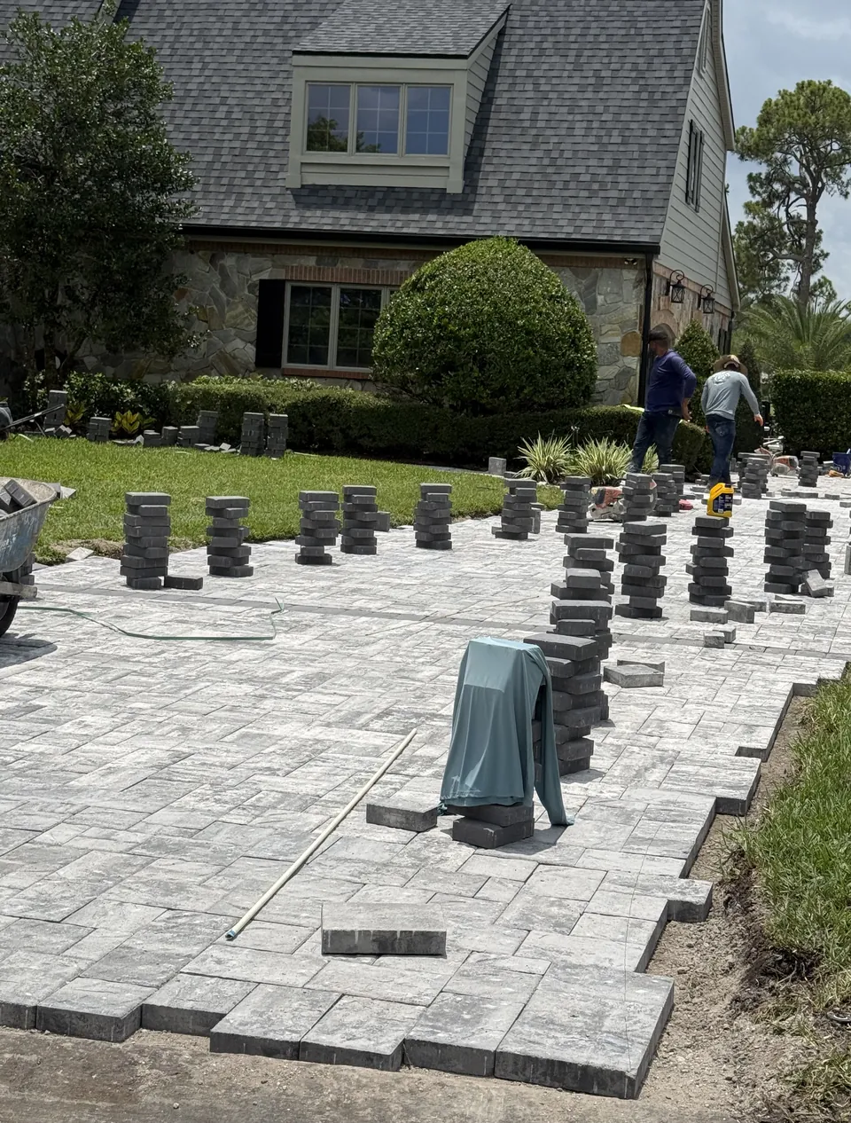 Paver driveway installation in progress with stacked pavers staged on the compacted base and crew setting the field