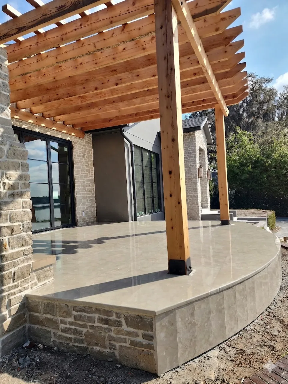 Raised curved terrace with large-format pavers, a stone-veneer retaining wall face, and a cedar pergola on a lakefront home