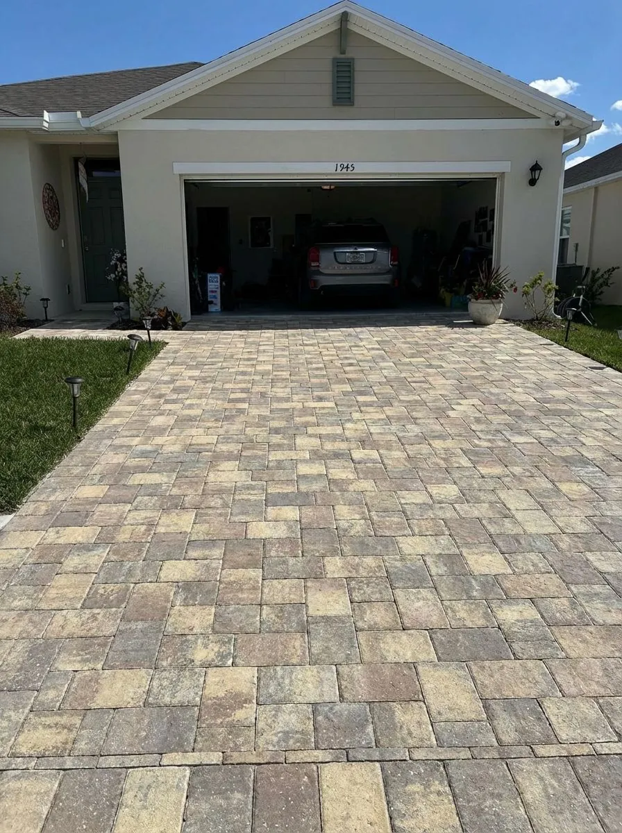 Tan and gray blend paver driveway in a random pattern, with solar path lights along the lawn edge