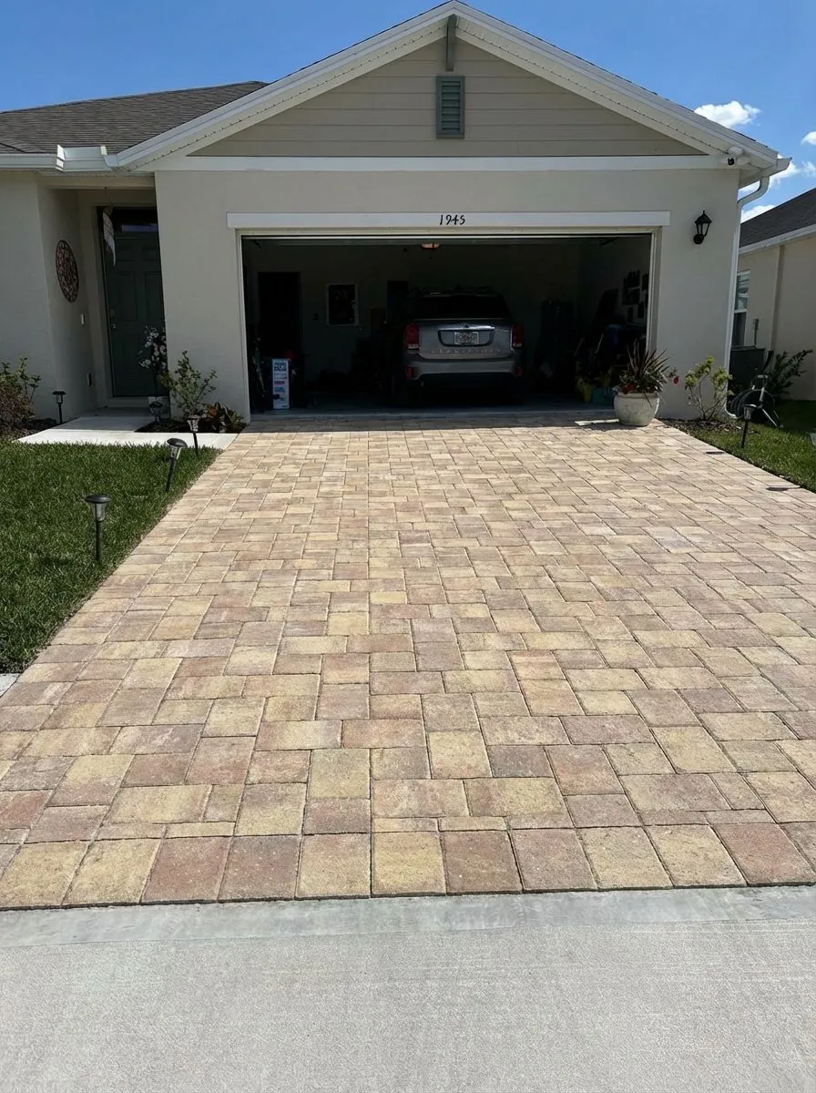 Tan blend paver driveway meeting a poured concrete apron at the street, in front of a two-car garage