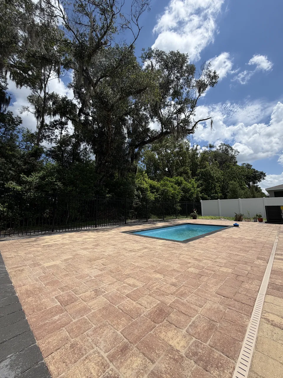Tumbled travertine-look paver pool deck with a drainage channel around a rectangular pool under mature oaks